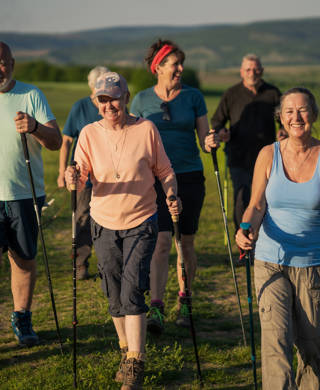 Retired friends are walking together in the country using nordic sticks accompanied with their pet dogs