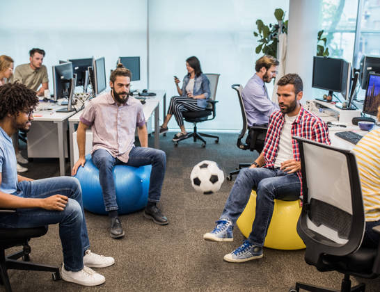 Young computer programmers having fun while playing with soccer ball in the office.