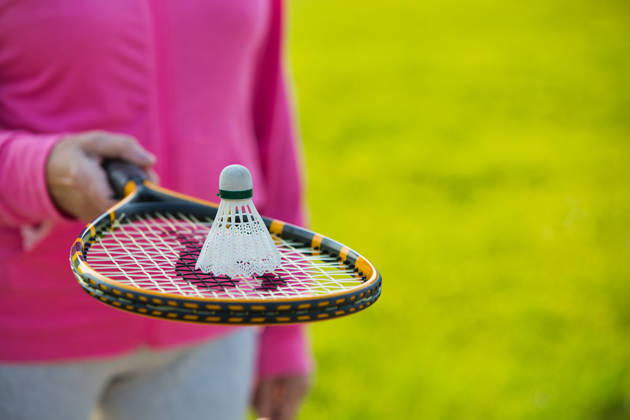 Midsection of senior woman with shuttlecock on tennis bat in park