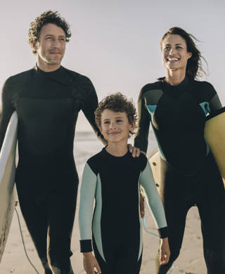 Close up of a family walking on the beach and carrying their surfboards