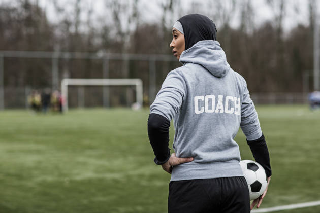 Jonge vrouwelijke voetbalcoach met hoofddoek op aan de rand van een voetbalveld