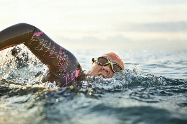 Determined mature woman swimming in sea. Female is in wetsuit doing water sports during sunset. She is representing healthy lifestyle.