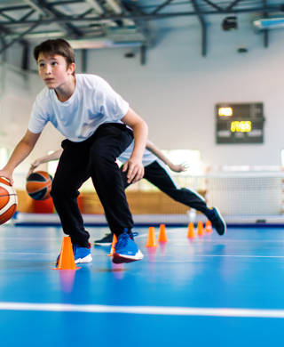 Studenten en hun coach basketten tijdens de turnles op school en de lerares kijkt toe.
