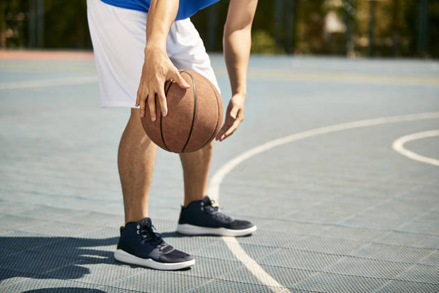 jonge basketter dribbelt met bal, enkel benen zichtbaar