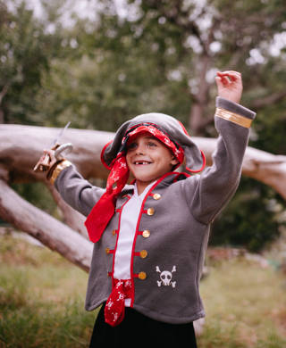 Excited little Boy dressed up as pirate grinning with toothy smile and missing some teeth. Fallen tree and log in the nature background