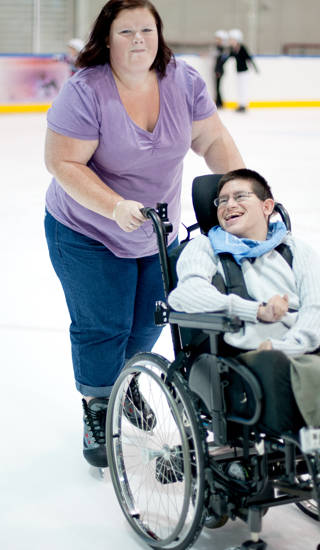 Jonge man in rolstoel wordt door dame vooruit geduwd op het ijs