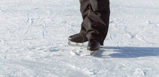 Men's legs in black skates close-up, standing on the rink facing the sun. Active winter holidays