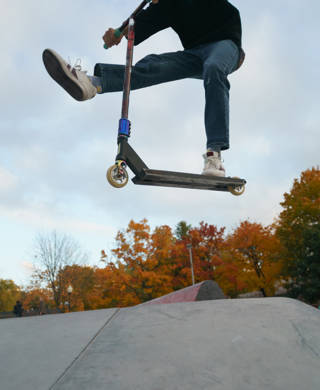 Teenager performs trick in the city skate  park. Push scooter. He is jumping. Extreme sports is popular among youth. View of park of body