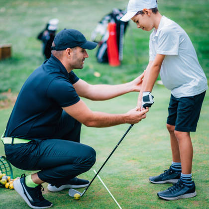Golf coach helpt jongen om stick goed vast te houden