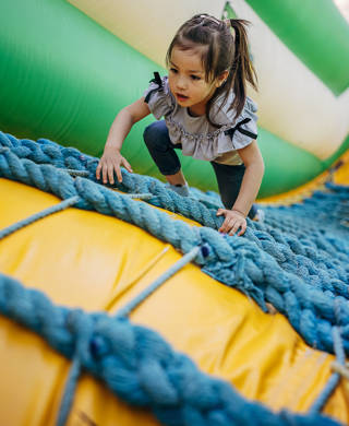 Cute little girl playing in climbing up inflatable bouncy castle in amusement park.