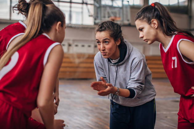 Vrouwelijke basketbalcoach in het midden van meisjesteam in sporthal
