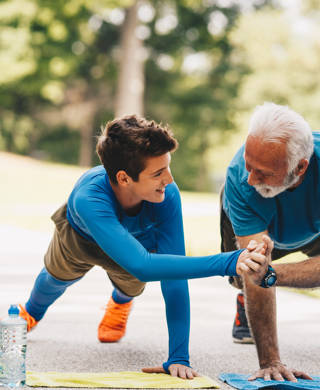 Granddad is doing exercises with his grandson in park. They are now finishing series of push ups. They had enough for today. Both of them are proud of themselves and progress they made today.