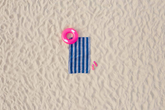 Striped beach towel, flip flops and swim ring on sand, aerial view