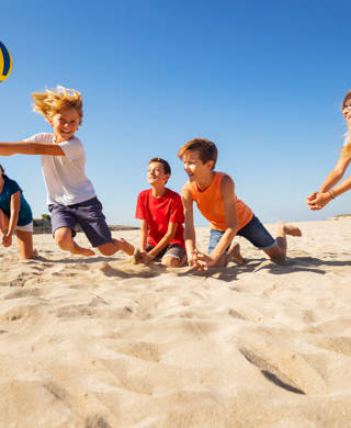 Groepje kinderen spelen volleybal op het strand, jongen slaat op