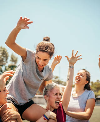 Female soccer players celebrating victory after soccer game, carrying player of the game on shoulders and cheering together