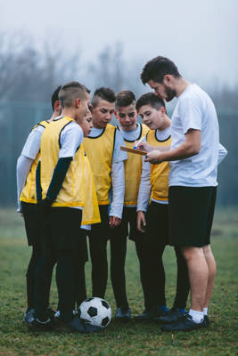 Tieners en trainer in cirkelgesprek op voetbalveld